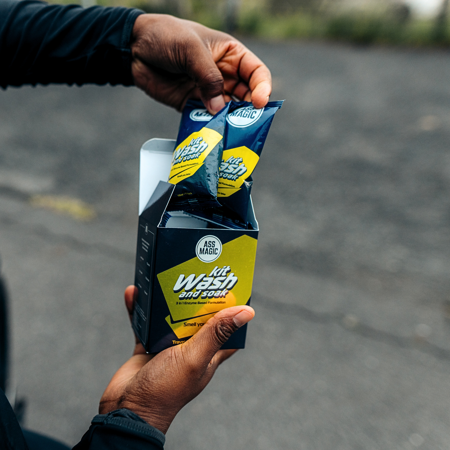 Person removing a sachet from a box of ASS MAGIC Kit Wash and Soak, an enzyme-based solution for washing sports clothes and eliminating sweat odour.
