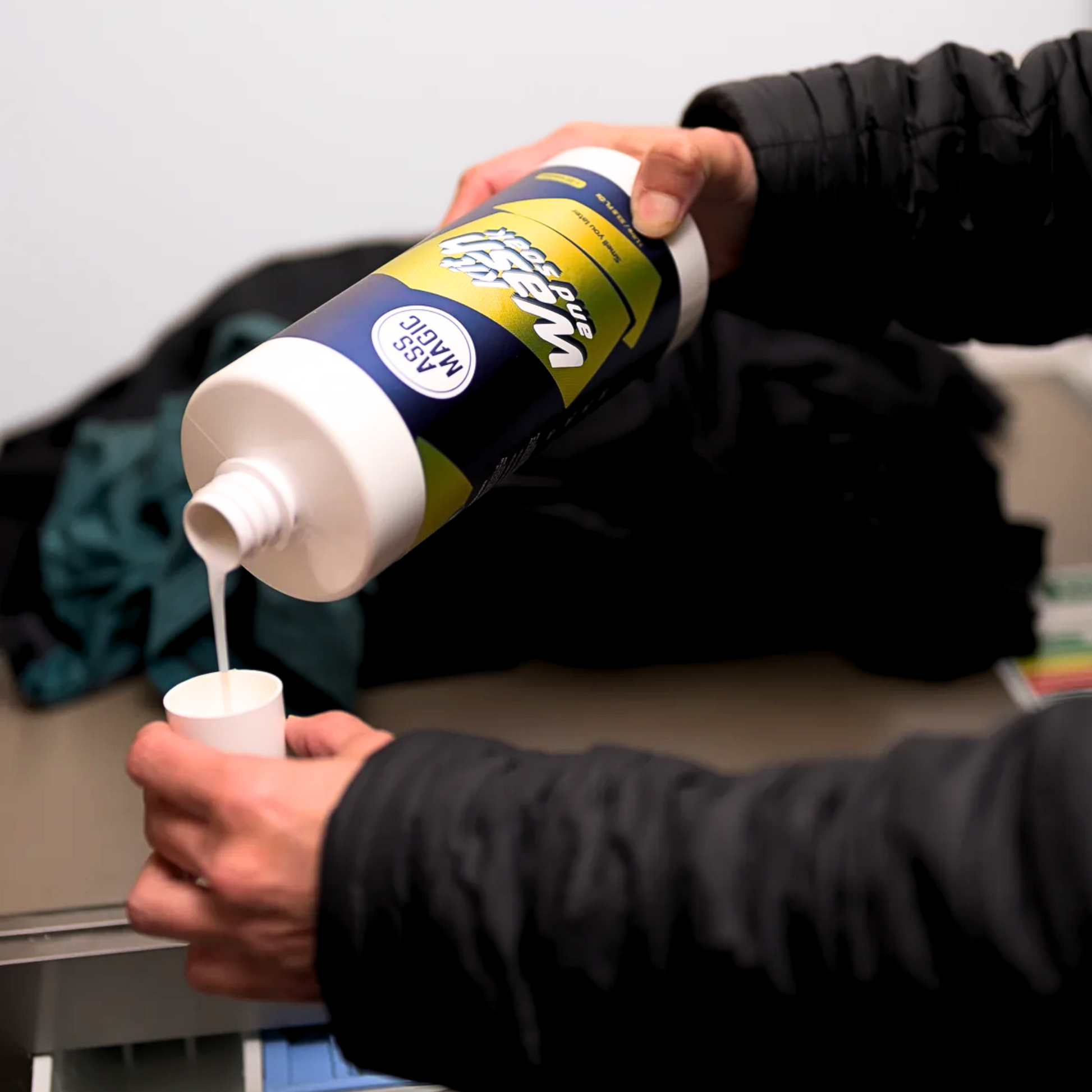 Pouring ASS MAGIC Kit Wash into a washing machine – enzyme-based formula for deep cleaning of performance kit and activewear.